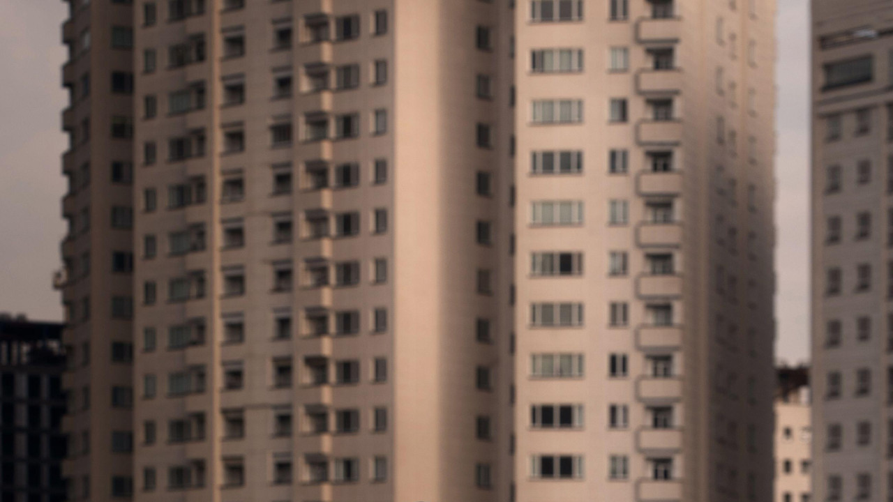 Prekrivena crnom plastikom, žena u crvenoj majici, crnim pantalonama i cipelama stoji ispred nebodera, dozvoljavajući crvenom balonu u obliku srca da padne na zemlju.