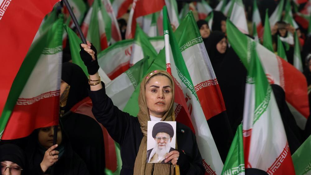 An Iranian woman waves the Iranian national flag while holding a picture of Iranian supreme leader Ayatollah Ali Khamenei 