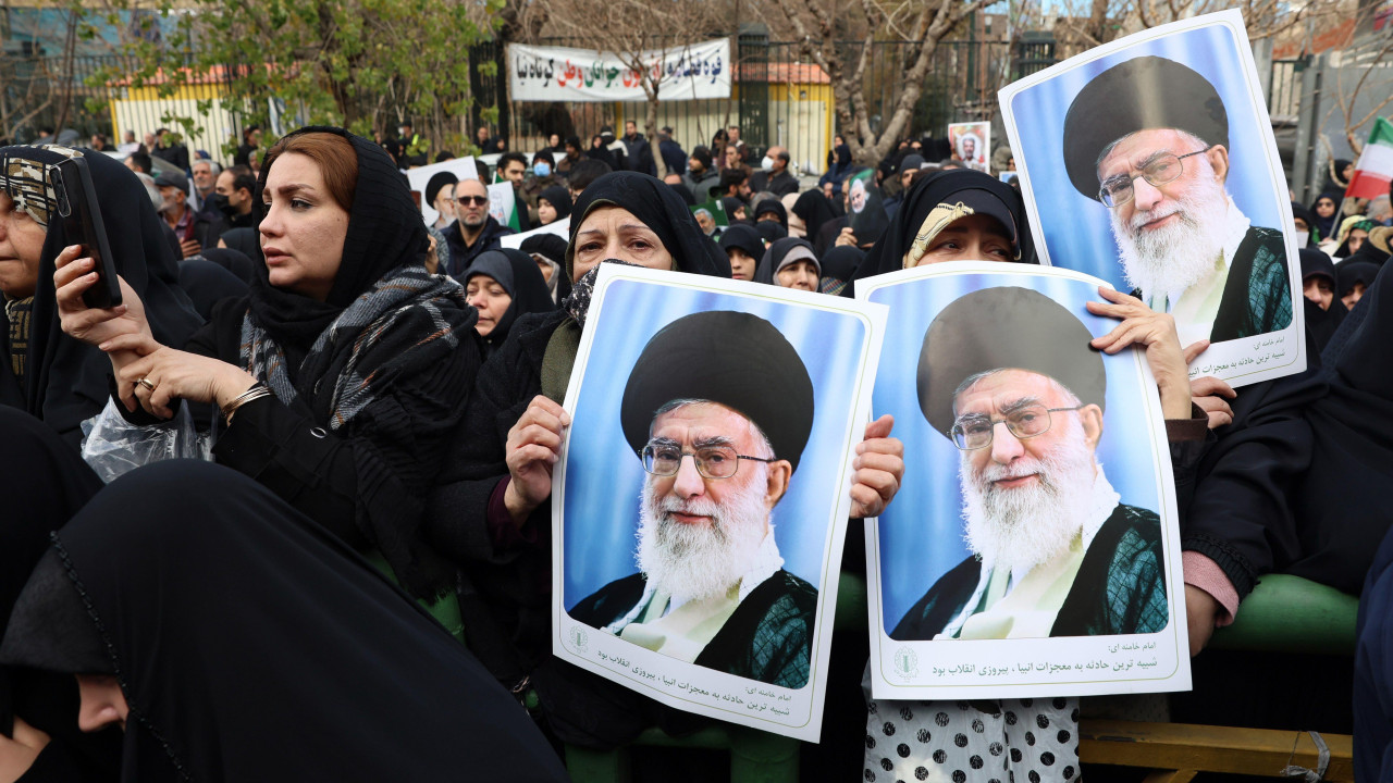 Woman dressed in black robes gather in an outdoor public area on 14 January 2026. Three of them are holding posters of Khamenei.