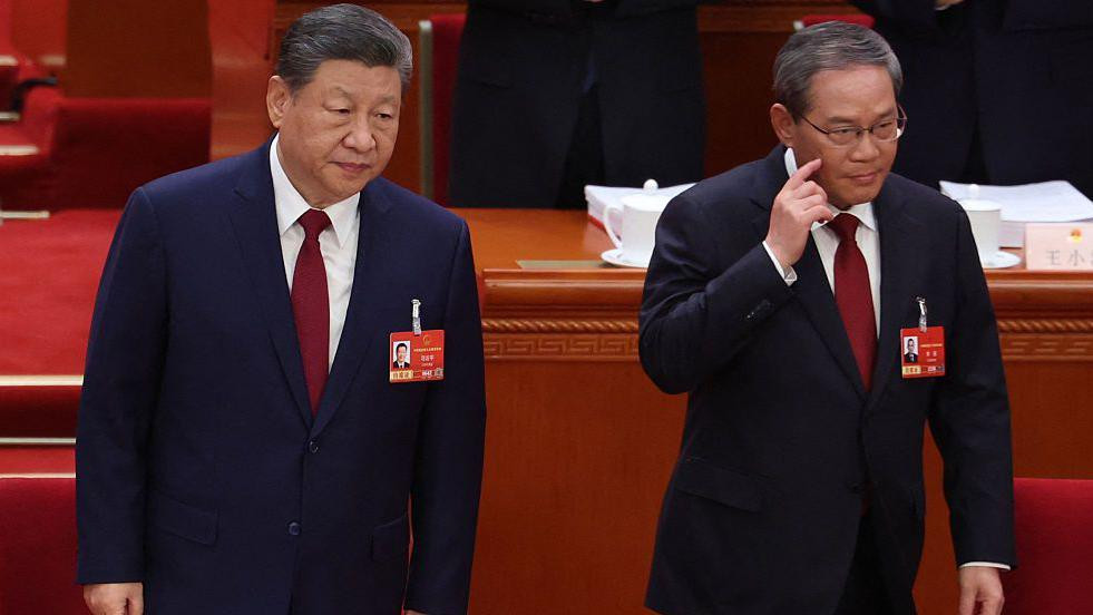 
                    China's President Xi Jinping standing next to Premier Li Qiang as they take their seats at the opening session of the National People's Congress (NPC) at the Great Hall o