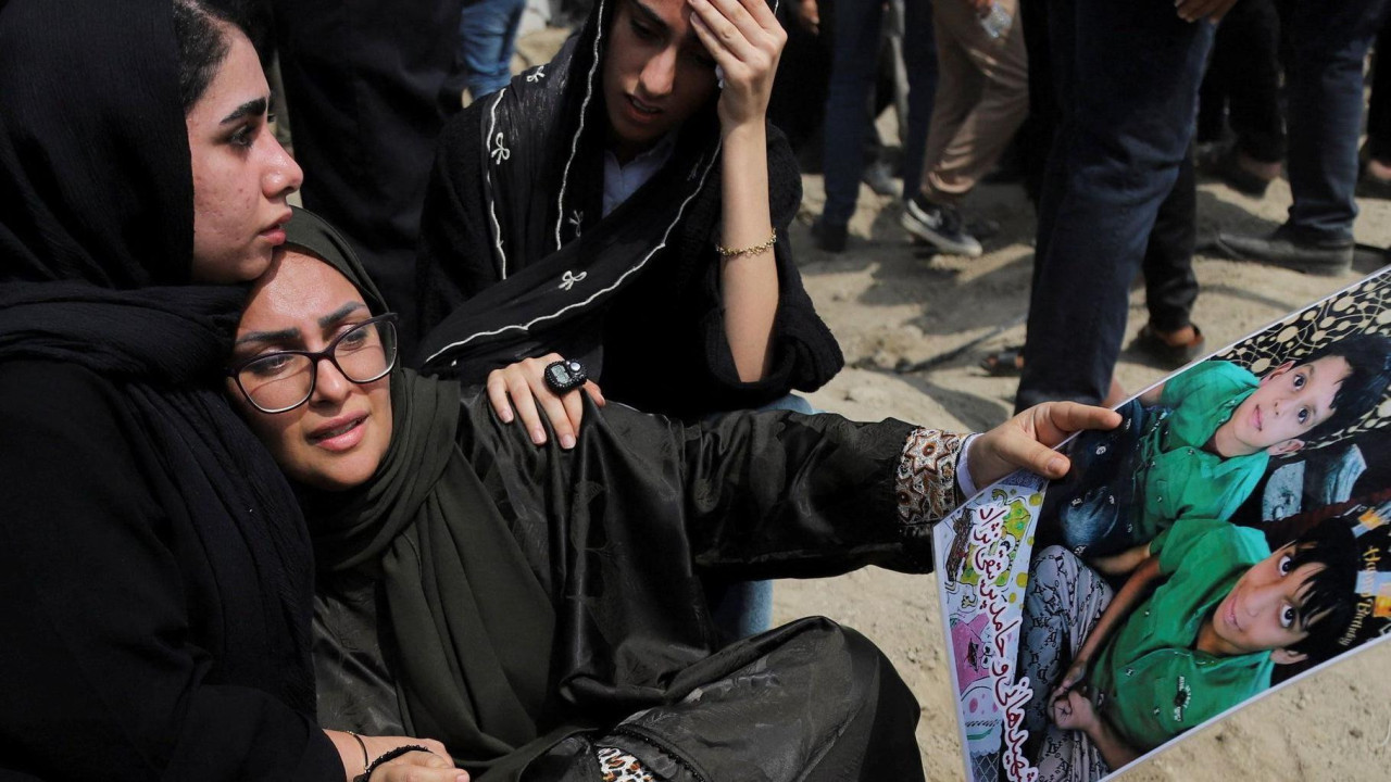
                    A woman holding a picture of two children is hugged by another woman during a funeral for those killed in an airstrike on a school on 3 March 2026. Image by Amirhossein K