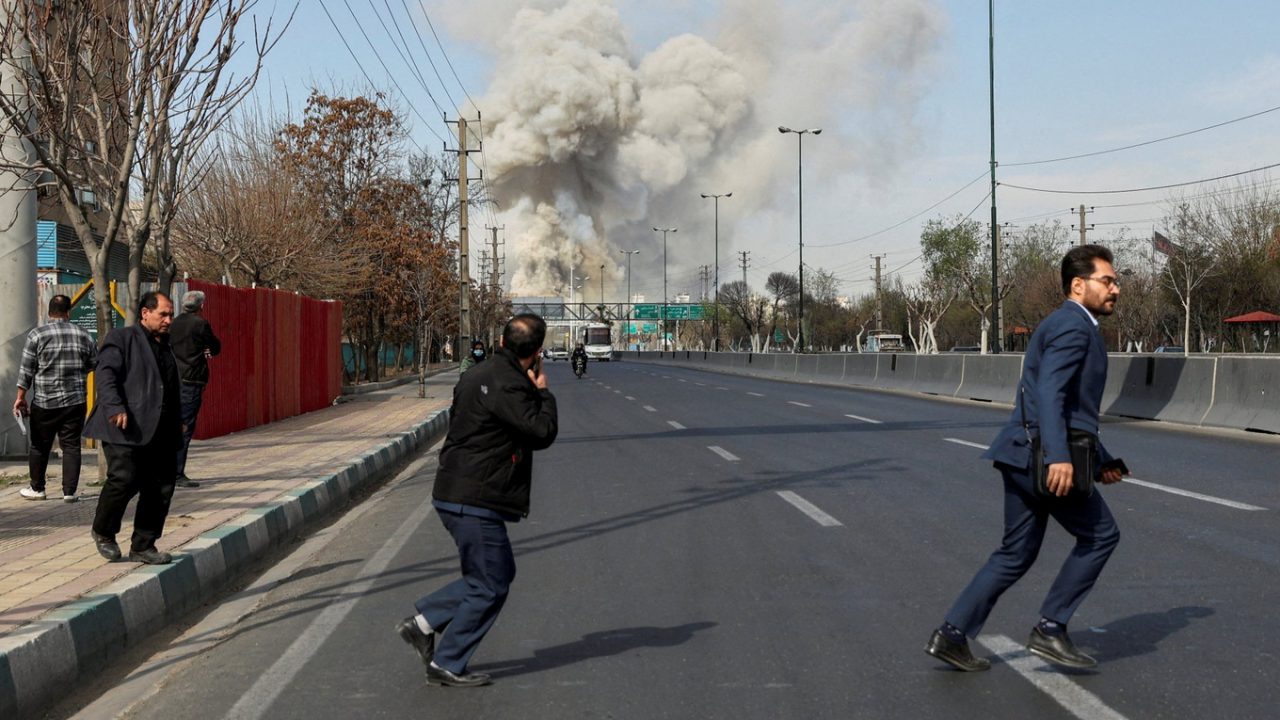 Ljudi pretrčavaju ulicu dok s eu pozadini vidi dim od eksplozije rakete