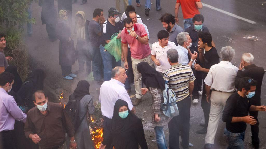 Demonstranti se okupljaju tokom protesta 2009. godine, pri čemu neki pojedinci duvaju dim jedni drugima u oči kako bi ublažili efekat suzavca. 