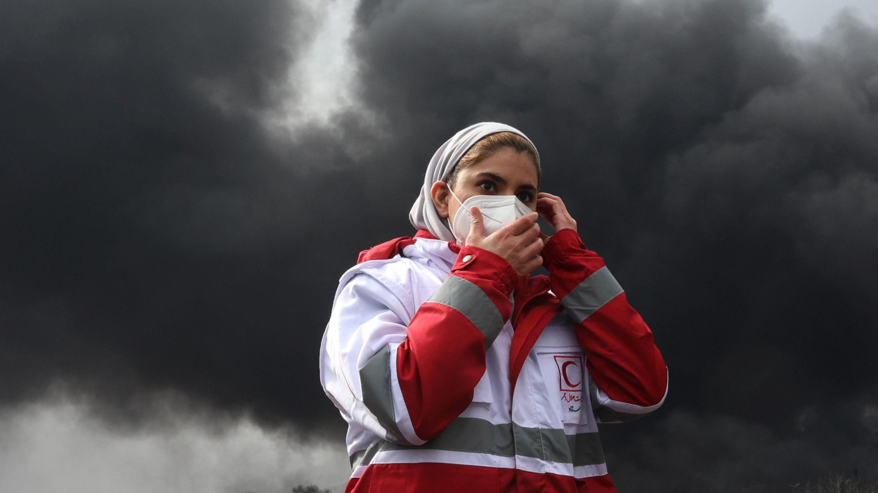 teheran, iran, pogođena naftna skladišta u iranu, žena nosi masku preko lica, a iza nje je gust dim