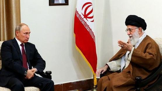 Ruski predsednik Vladimir Putin, u crnom odelu i sa crvenom kravatom, razgovara sa iranskim vrhovnim vođom ajatolahom Alijem Hamneijem. Iranska zastava je u pozadini, između njih dvojice 