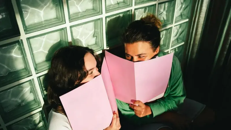 Dve devojke se smeju i prekrivaju lice roze listovima