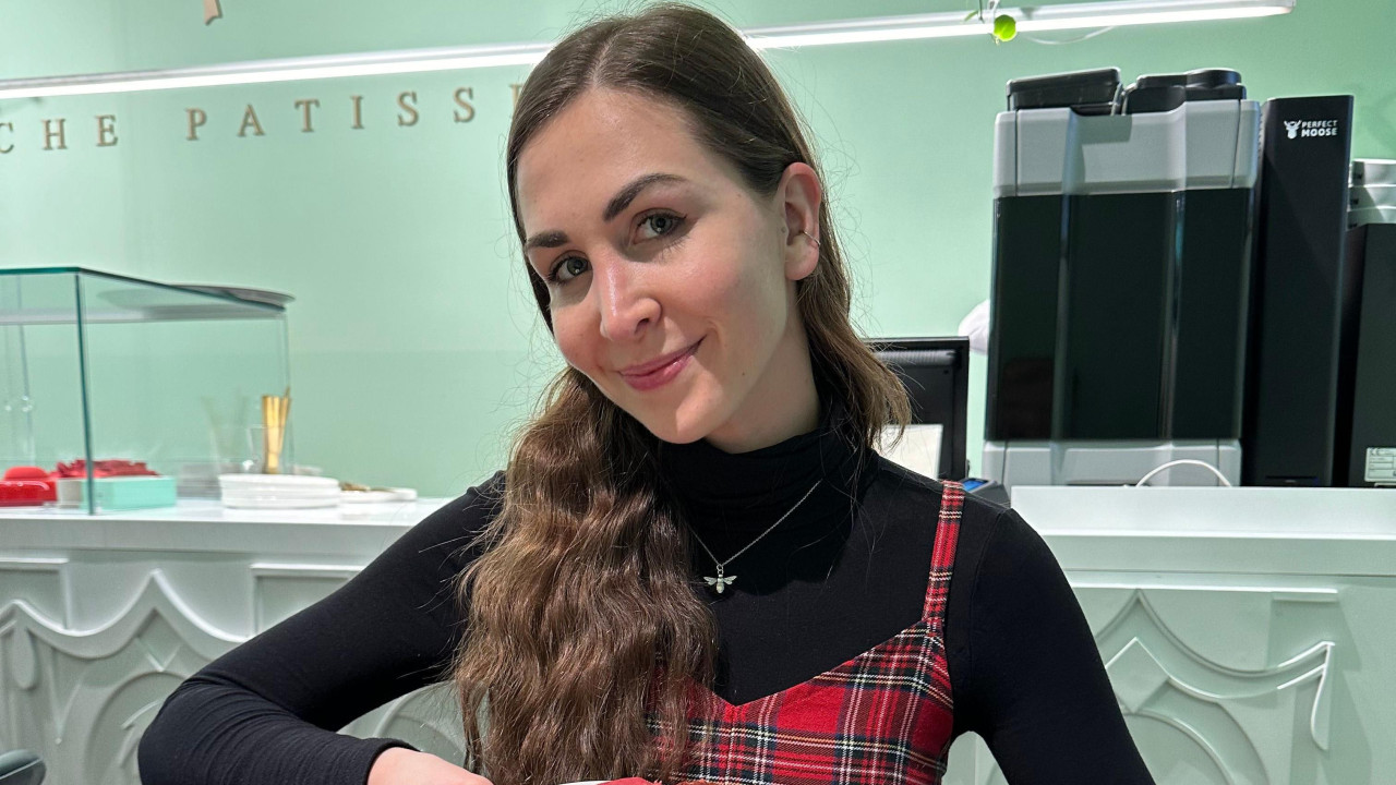 Žena sa dugom smeđom kosom, u crnoj rol kragni i kariranoj haljini, osmehuje se u kameru