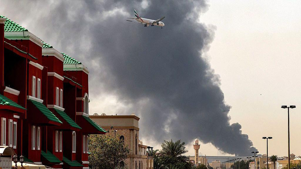 avion leti iznad dubaija, u pozadini se vidi dim posle iranskog napada