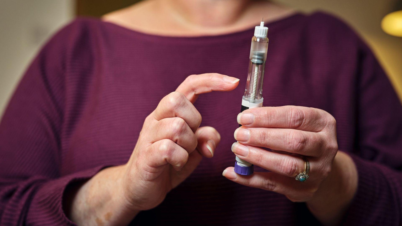 A woman in a burgandy top holds a weight loss injection pen