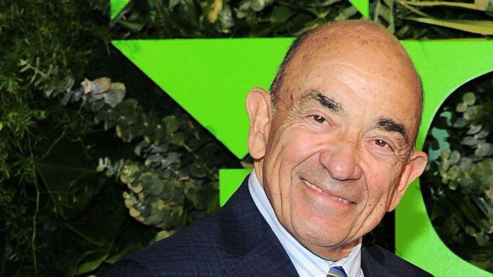 Sudija Alvin Helerštajn u odelu i prugastoj kravati, iza njega zelena zvezda i žbunje