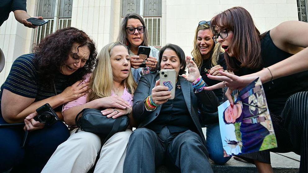 Grupa žena sedi na stepenicama i gleda u telefone