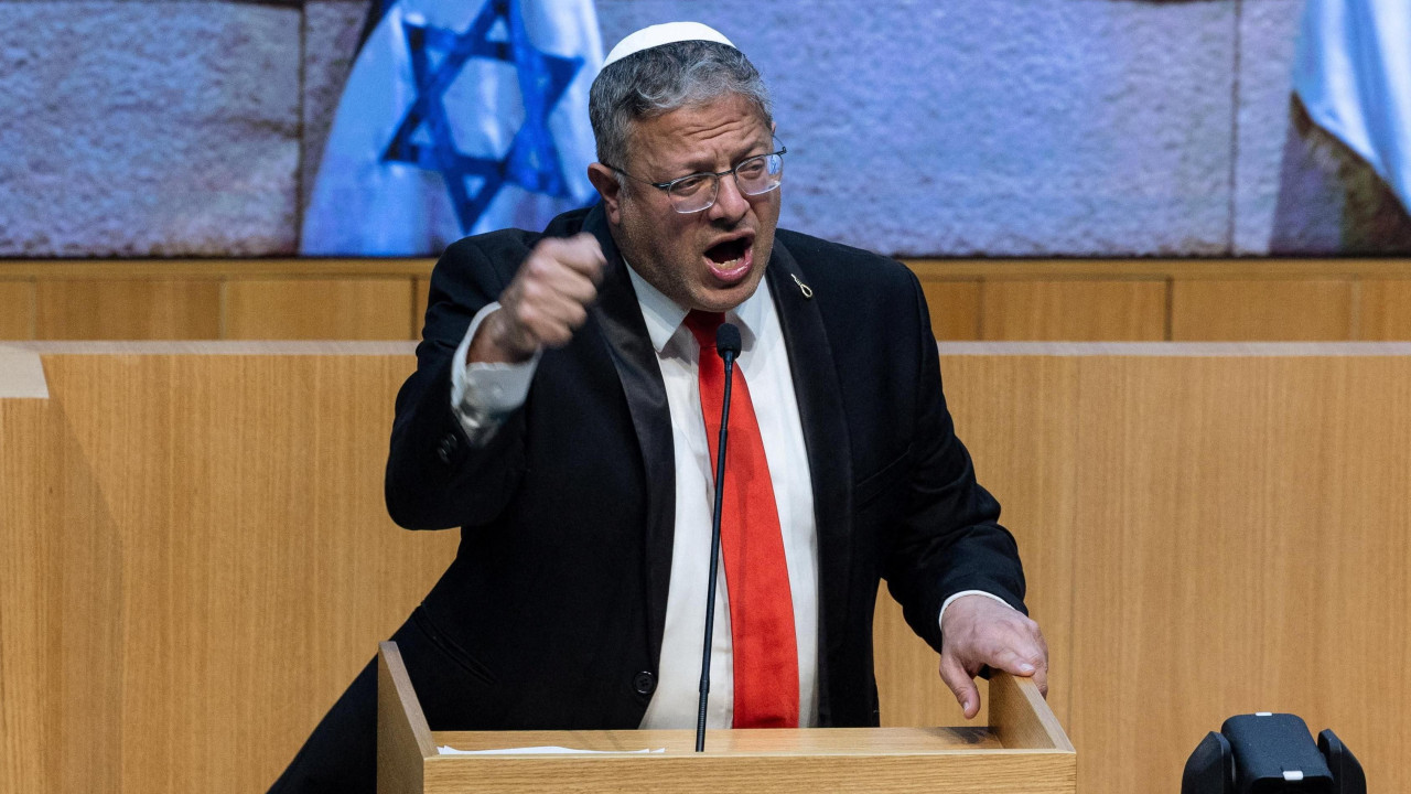 Itamar Ben-Gvir, u crnom odelu sa crvenom kravatom, podignutom desnom rukom, za govornicom