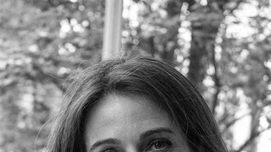 Crno-bela fotografija Ejmi Dikson koja gleda u kameru, ima belu blizu i ogrlice