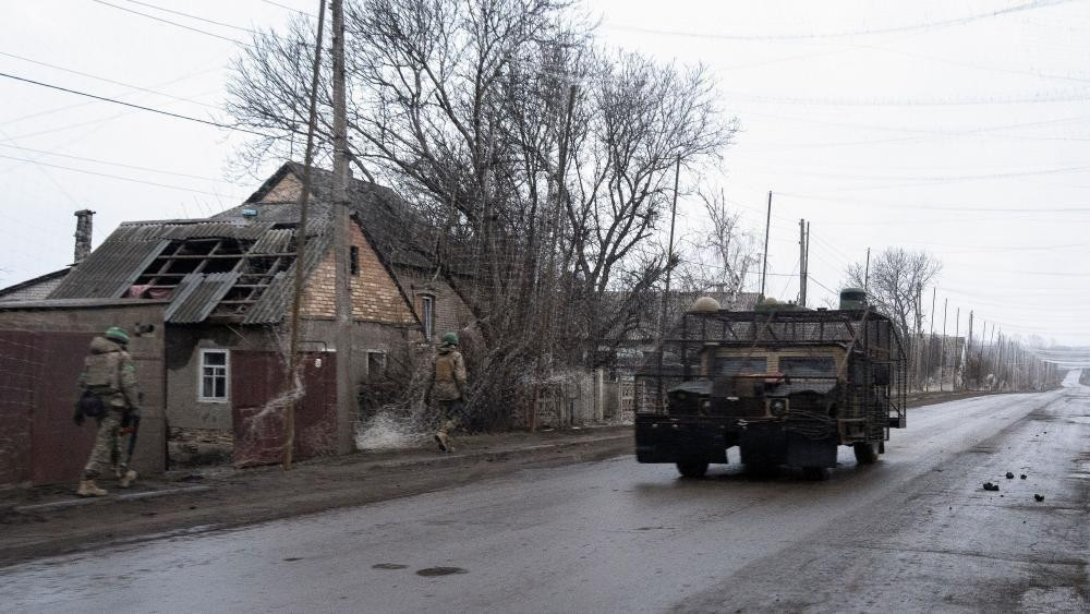 Vozilo protiv dronova na putu i dva vojnika koji prolaze trotoarom pored razrušene kuće