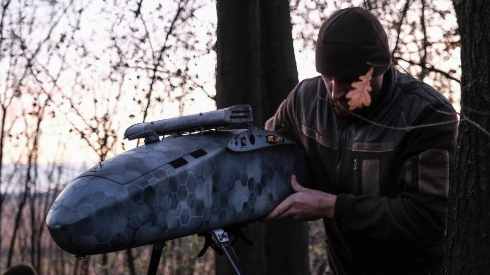 Pilot u vojničkoj uniformi sklapa bombarderski dron u šumi