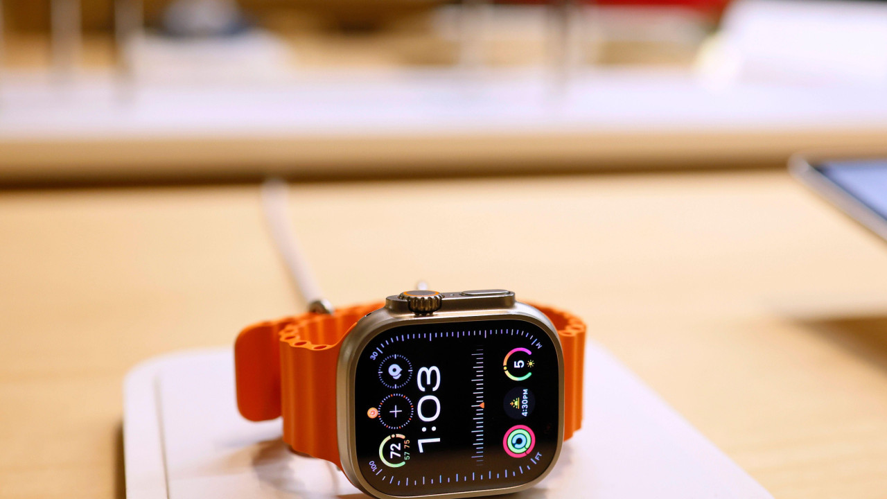 Epl sat sa crnim brojčanikom i narandžastim kaišem, na stolu. Pokazuje 1:03.