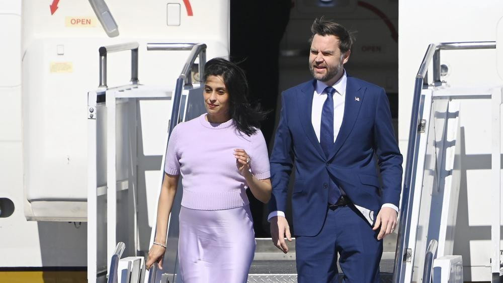 A man and woman in lilac walk down steps from a plane