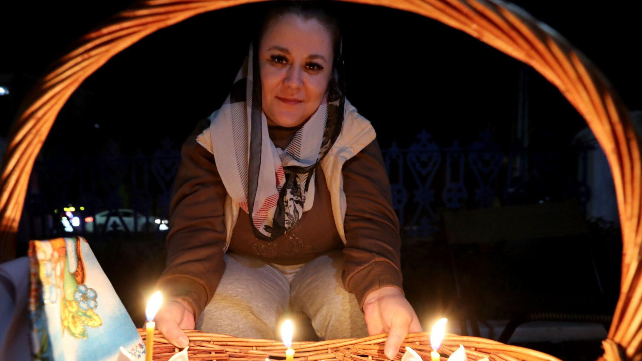 Devojka sa maramom preko kose drži drvenu korpu u kojoj je nekoliko kolača, tri sveće i ofarbana jaja