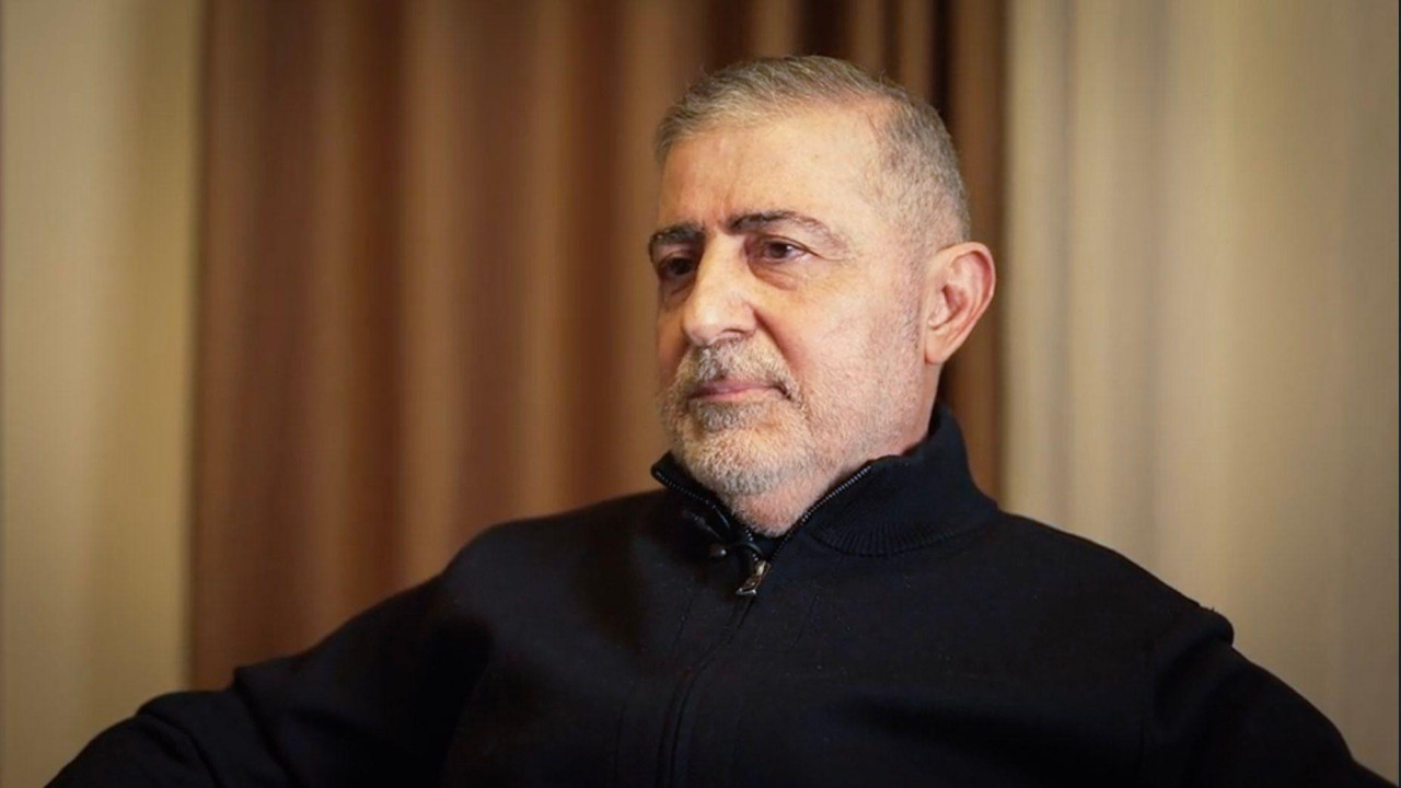 Čovek sedi na stolici u crnom džemperu i gleda u stranu kamere