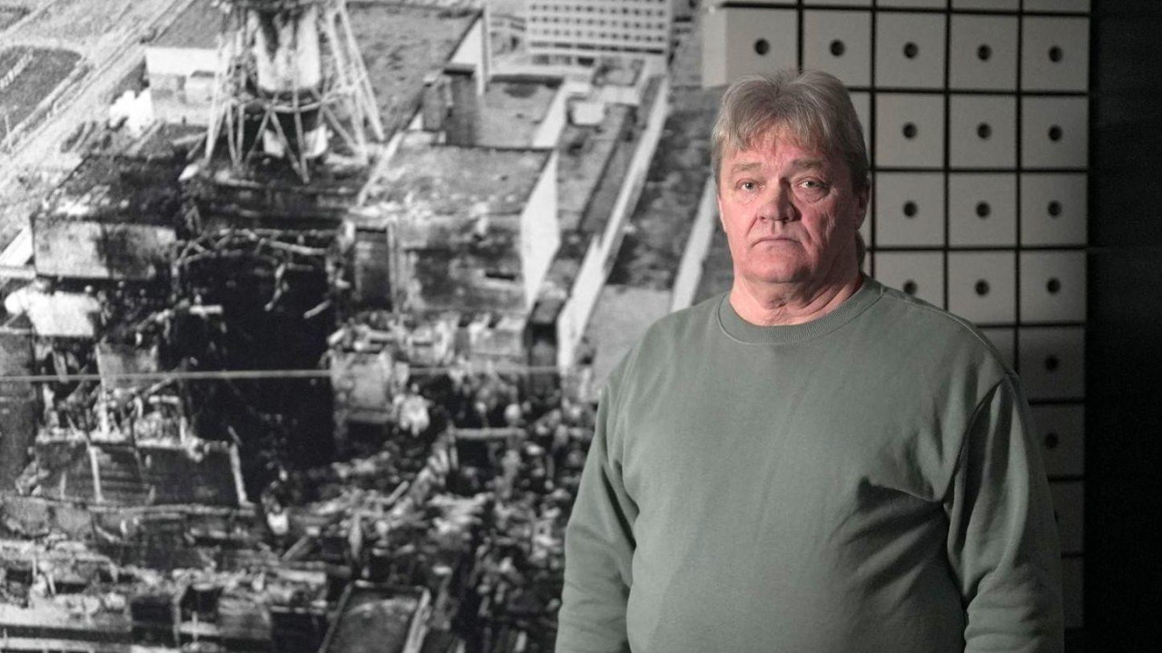 Muškarac pored  fotografije razrušene nuklearne elektrane