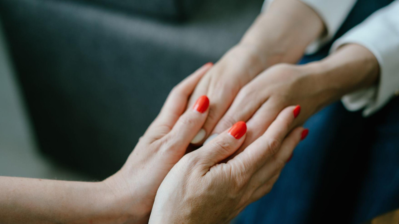 Two sets of hands - one with painted nails - hold on to each other in a close-up image. 