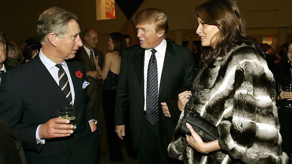 Čarls drži čašu pića dok razgovara sa Donaldom Trampom i Melanijom