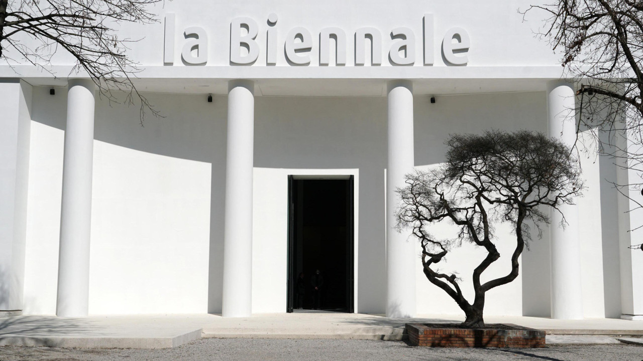 Bela zgrada sa natpisom „la Biennale“ i crnim drvetom ispred nje