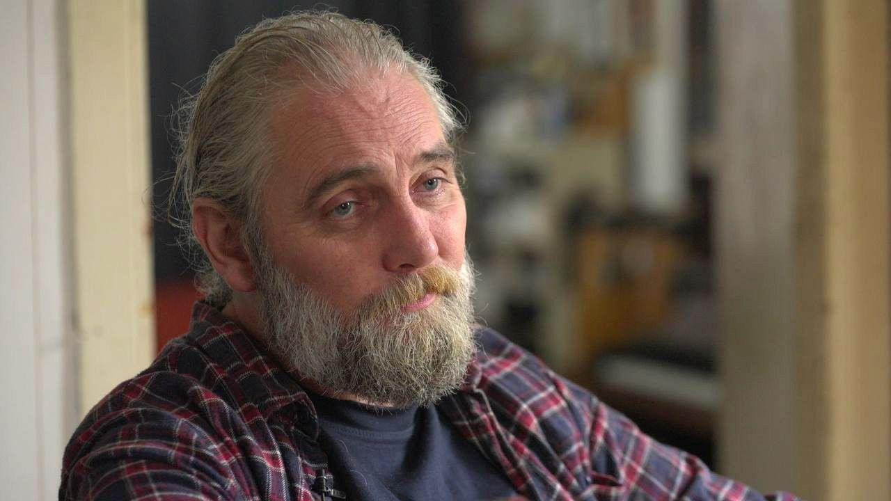 Adam Hurikan kod kuće, nosi kariranu košulju, ima sedu bradu