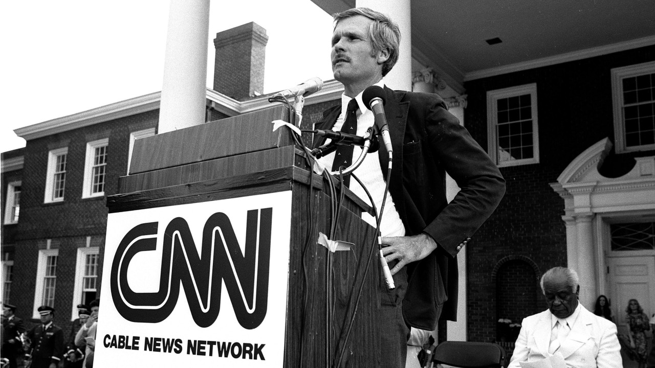Crno-bela fotografija Teda Tarnera kako stoji za govornicom sa logom CNN-a na lansiranju u Atlanti, Džordžija, 1. juna 1980. godine