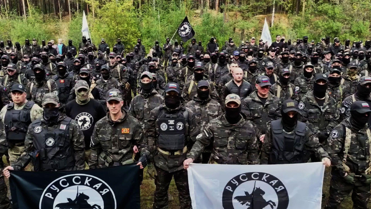Više desetina muškaraca u vojnoj uniformi drže zastavu na kojoj je vitez na konju 