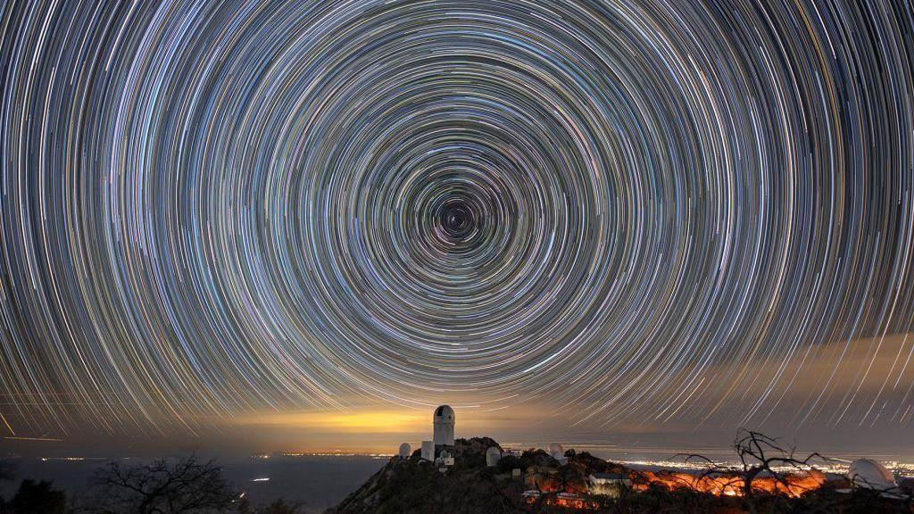 Noćna fotografija neba prikazuje zvezdane tragove koji se spiralno vijugaju preko teleskopa Majal u kojem se nalazi DESI. 