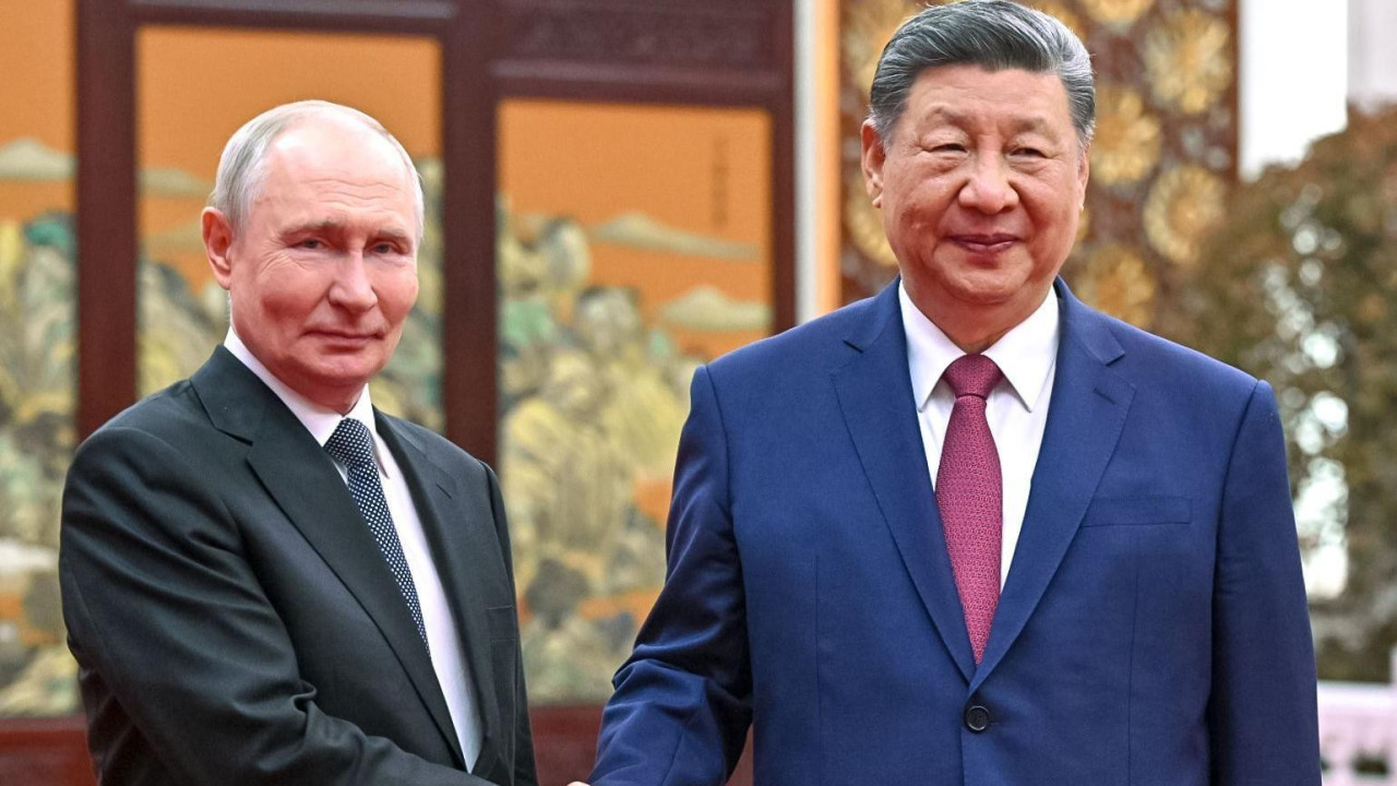 Putin in a dark suit, white shirt and polkadot tie shakes the hands of Xo in a navy suit, red tie and white shirt. The two leaders meet a tea ceremony. 