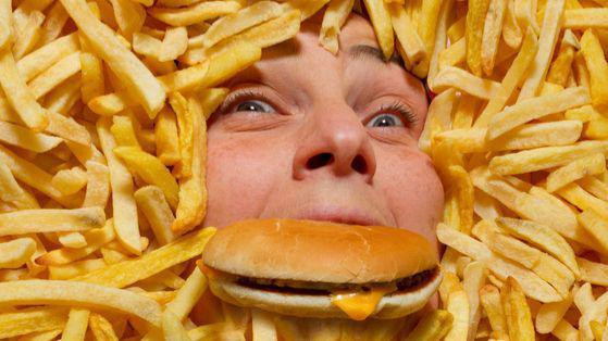 Čovek okružen krompirićima jede hamburger