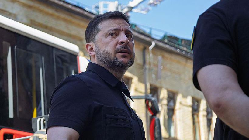Vladimir Zelenski u crnoj majici, uslikan napolju, dok gleda u daljini