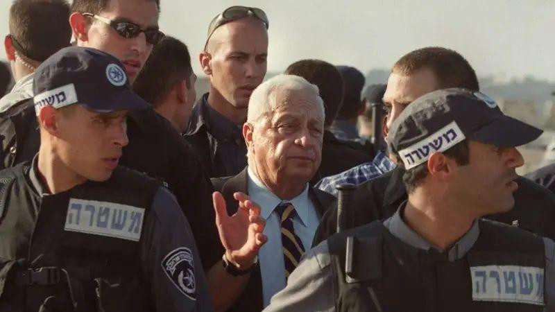 Tadašnji lider izraelske opozicije Šaron okružen čuvarima dok napušta prostor na kome se nalazi džamija Al Aksa 2000. godine