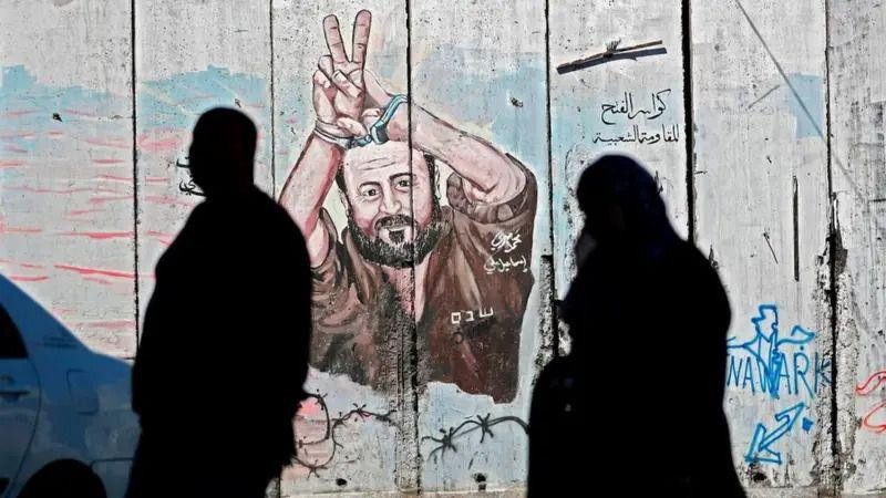 Dvoje ljudi prolaze pored grafita koji prikazuje palestinskog zatvorenika Marvana Bargutija