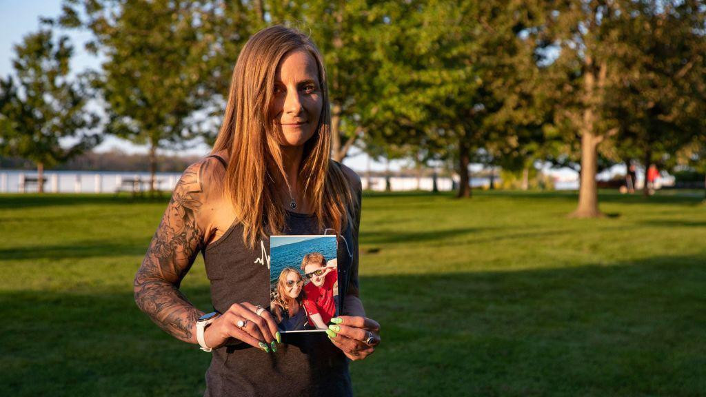 Žena u crnoj garderobi uslikana na zelenoj površini u rukama drži sliku na kojoj je dvoje ljudi