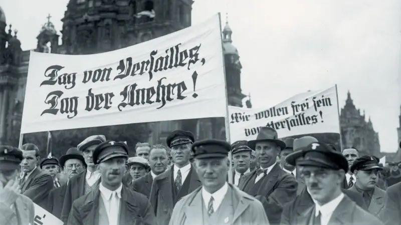 Grupa muškaraca drži transparente. Neki nose ravne kape, dok većina nosi sakoe i kravate.  