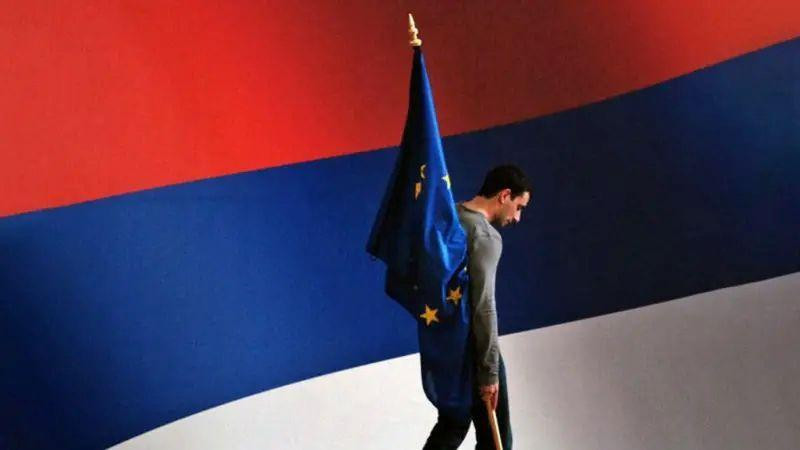 muškarac drži zastavu EU dok prolazi pored zastave Srbije