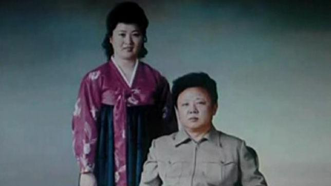 Ko Jong Hui, u ljubičastoj i zelenoj korejskoj haljini, stoji s leve strane. Kim Džong Il sedi 
