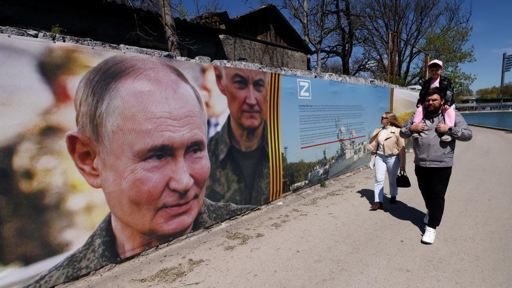 Muškarac sa decom šeta pored plakata sa Putinovom fotografijom