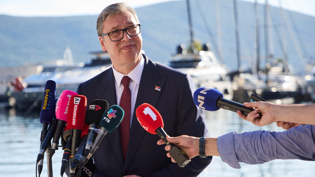 Aleksandar Vučić u odelu i kravati pred nekoliko mikrofona medija, daje izjavu, dok je iza njega more i jahte