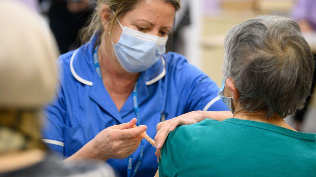 medicinska sestra u plavoj uniformi daje vakcinu starijoj ženi