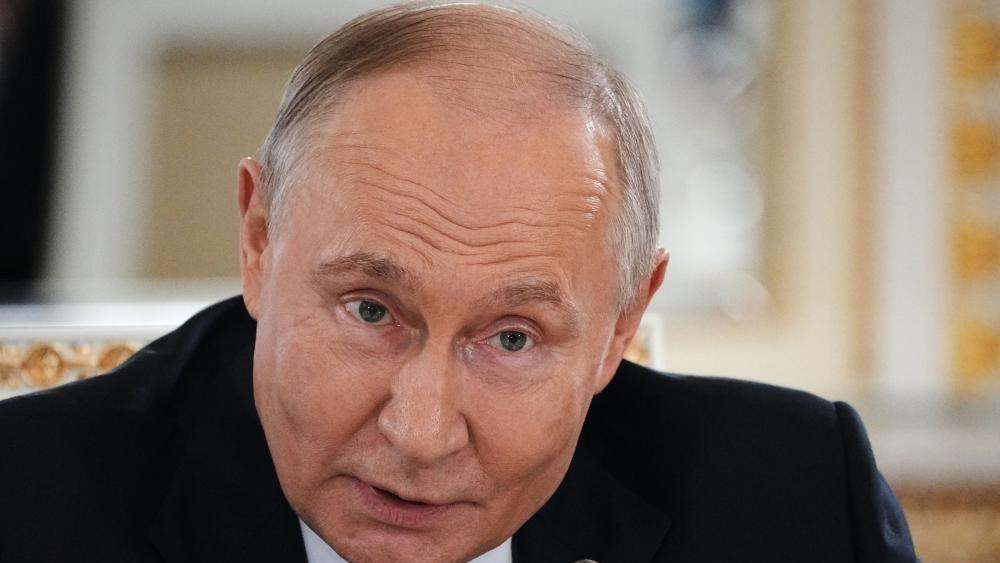 Putinu tamnom odelu sedi za stolom i govori