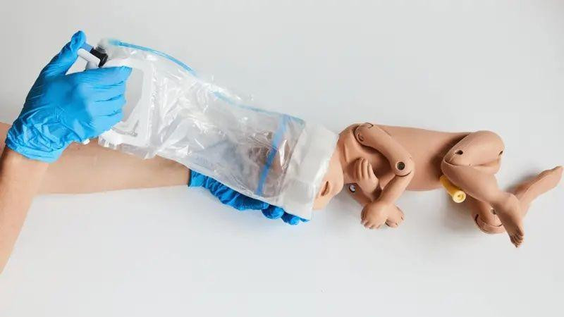 Lutka bebe i plastični uređaj, poput kese, oko njene glave
