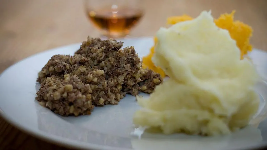 Hrana na belom tanjiru, u pozadini čaša vina