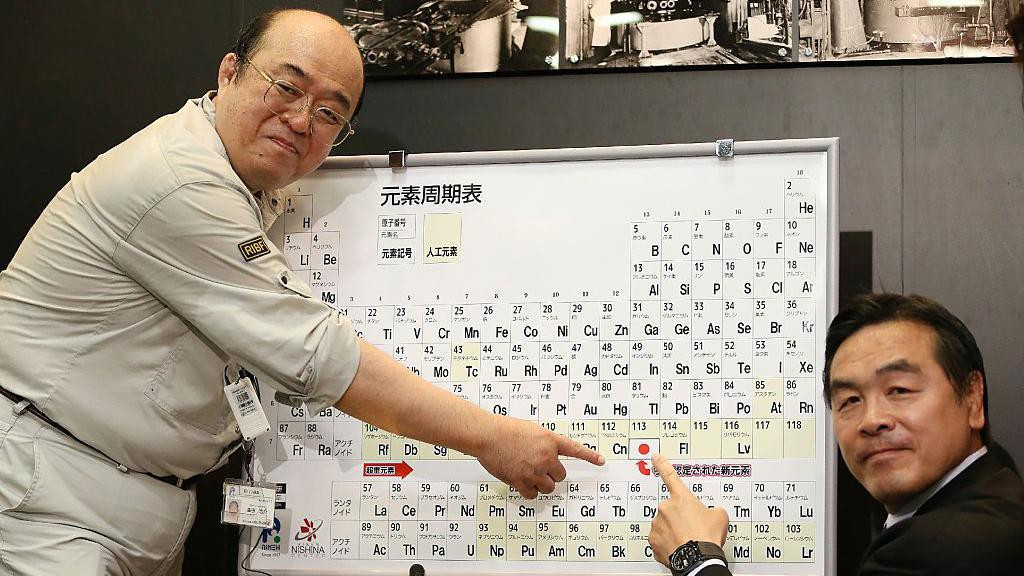 Dva muškarca pokazuju na uramljeni periodni sistem elemenata na broj 113, gde je i japanska zastava