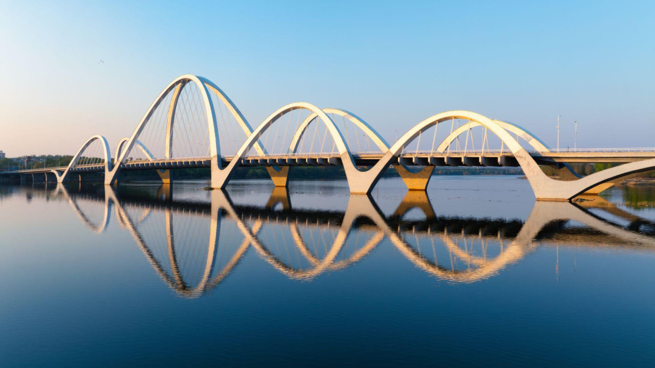 Fotografija mosta sa nekoliko zakrivljenih ivica koje se ogledaju u vodi