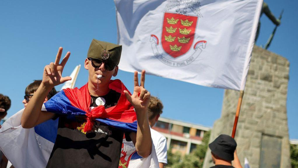 učesnik studentskog skupa u Kraljevu sa šajkačom, zastavom i tri prsta