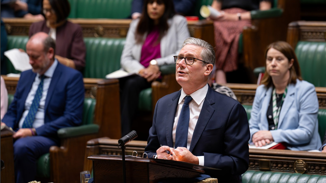 Premijer Velike Britanije u odelu i naočalama gleda nagore tokom govora u parlamentu